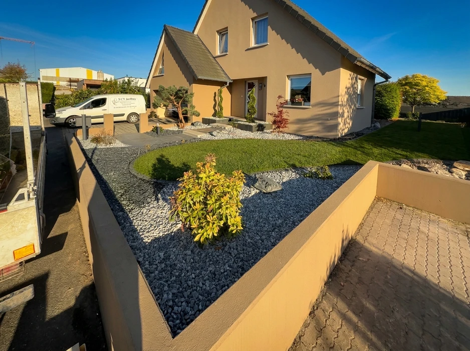 Jardin minéral moderne en façade de maison, aménagement paysager avec graviers blancs type marbre concassé et ardoise noire, délimités par muret en béton enduit avec chaperon en granit