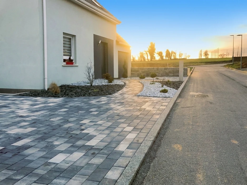 Allée de jardin pavée en briques avec motif en chevrons, bordée de pelouse verte et plantations paysagères variées